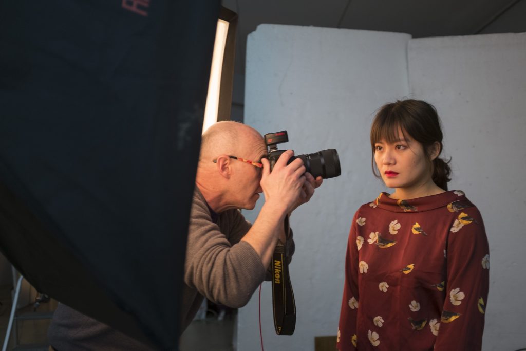 Un photographe professionnel prend un portrait d'une modèle en studio, avec des éclairages et un fond neutre.