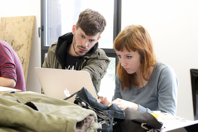 Un étudiant pointe du doigt un écran d'ordinateur portable tout en expliquant quelque chose à une étudiante attentive dans un environnement de travail collaboratif.