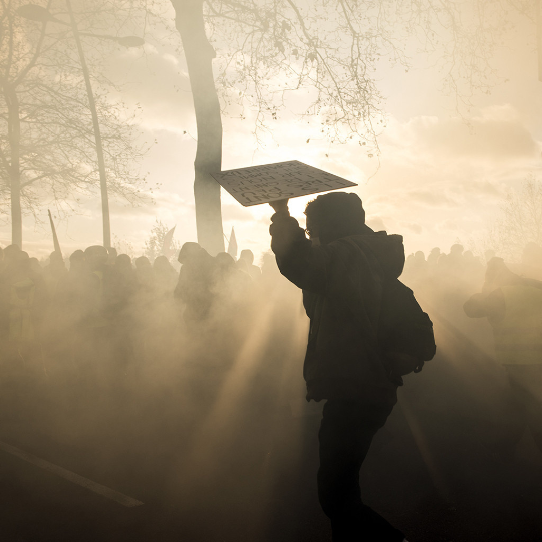 un jeune homme avec une capuche se protège avec un panneau lors d'une manifestation sous une lumière filtrante c'est un photographe de presse